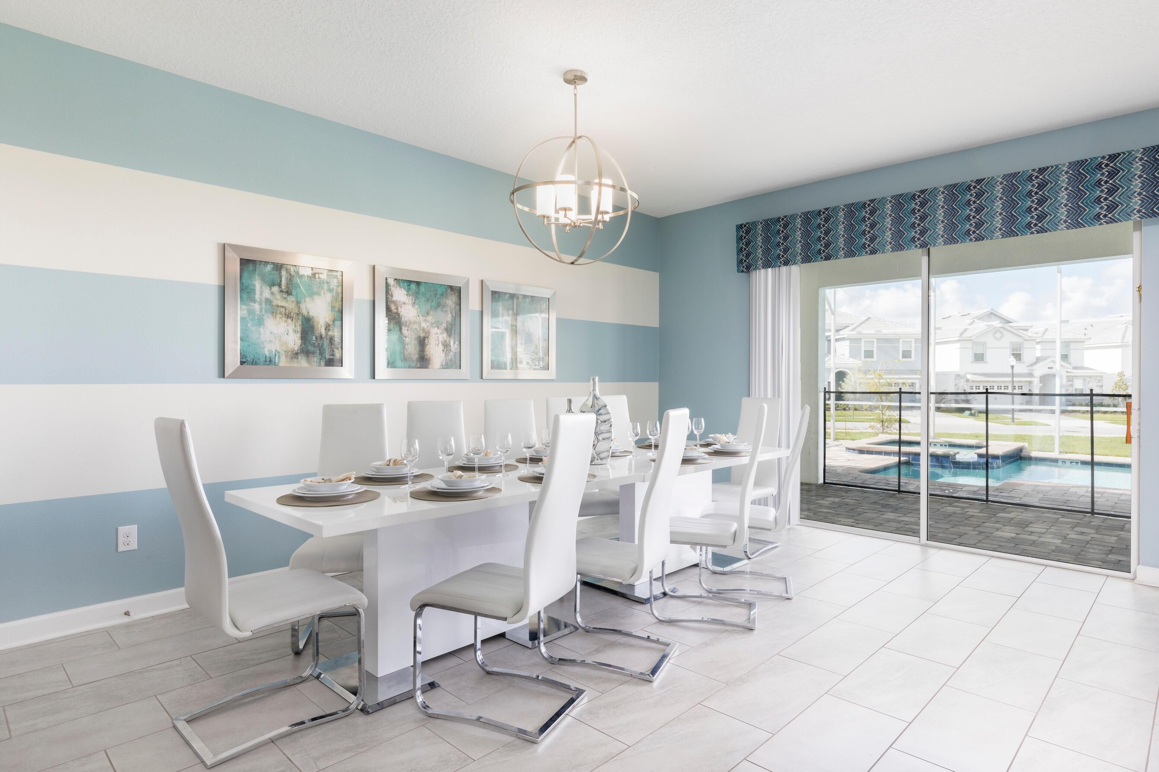 A dining area with a white table and chairs, a chandelier, and artwork on the wall.