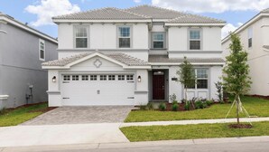 A two-story residential house with a white exterior, a garage, and a small front yard with a young tree. - 1668mvd - Non-renting 6-12-2022 The Retreat at Championsgate (Davenport)