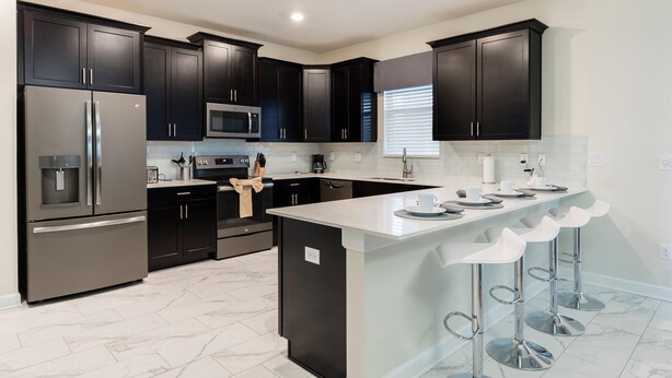 A modern kitchen with dark cabinetry, stainless steel appliances, and a central island with bar stools. - 1668mvd - Non-renting 6-12-2022 The Retreat at Championsgate (Davenport)