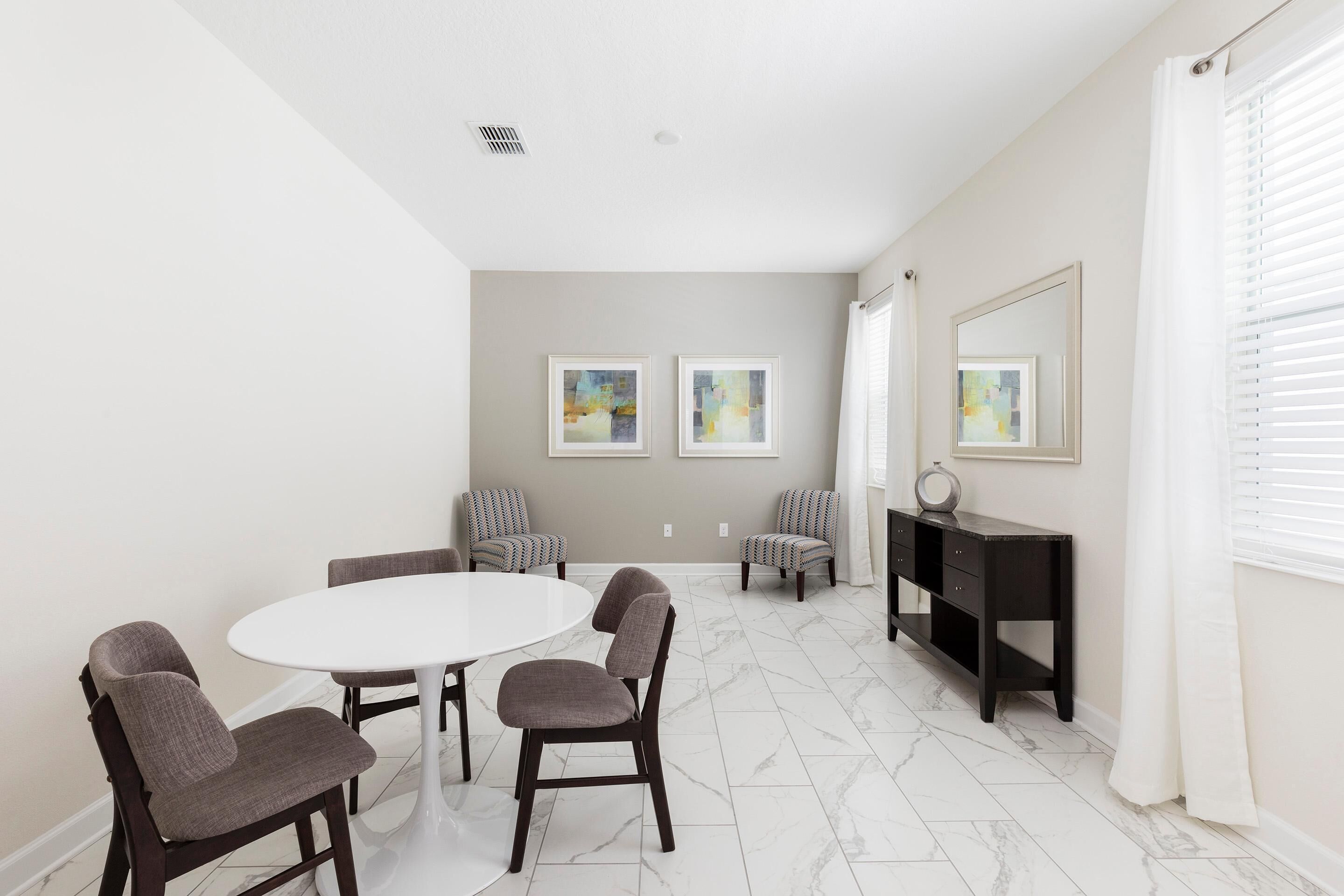 A dining area with a round table and four chairs, a dark wooden console table, and two framed abstract paintings on the wall.