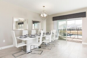 Un espace de salle à manger moderne avec une longue table, des chaises blanches et un lustre.