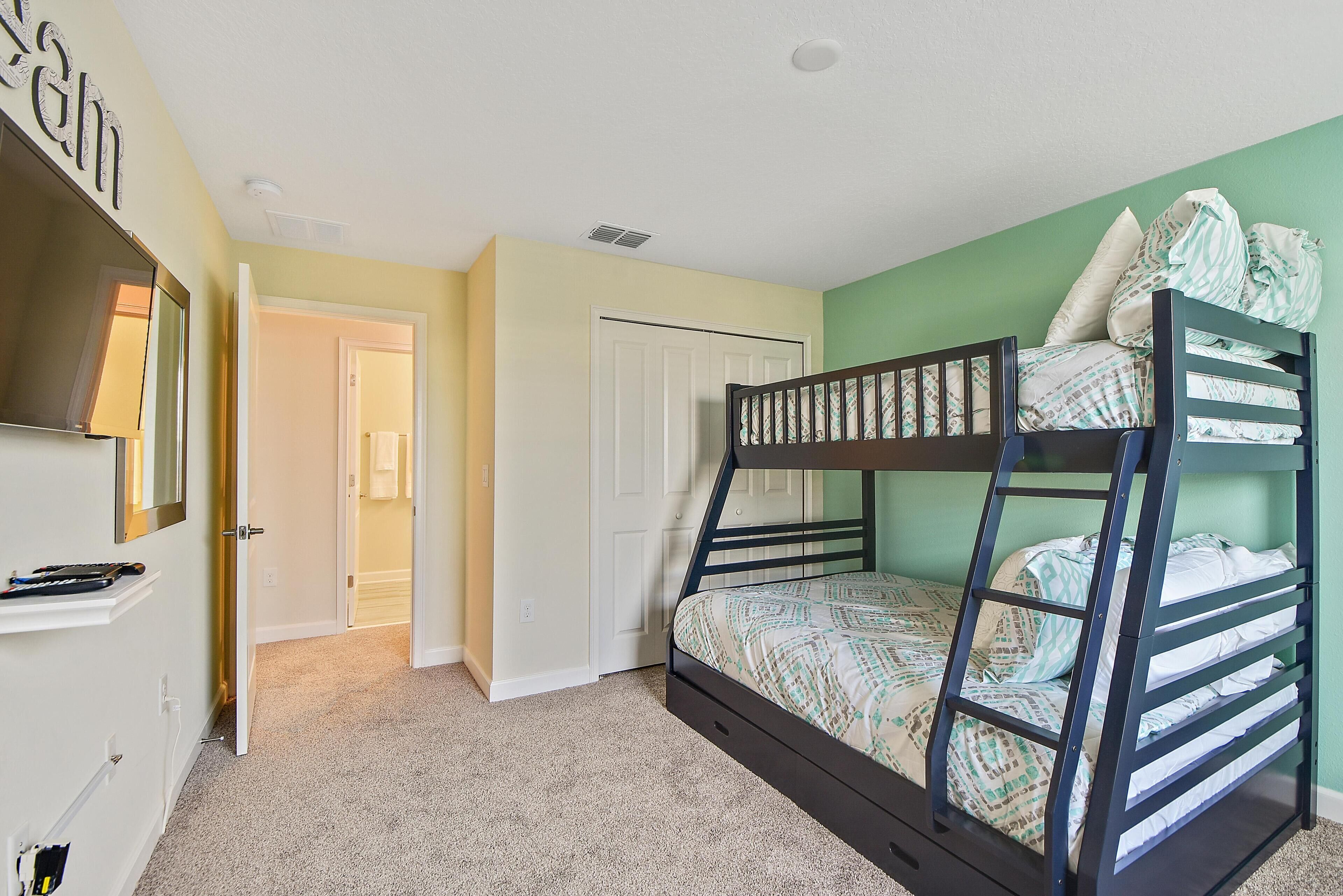 A bunk bed with a patterned bedspread, a white door, and a hallway leading to another room.