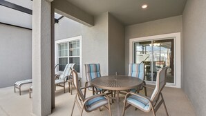 An outdoor patio with a round table and six chairs, a concrete floor, and a view through a glass door. - 1579mvd-the Retreat at Champions Gate (Davenport)