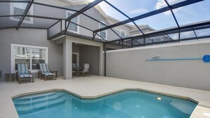 An indoor swimming pool with a glass ceiling, lounge chairs, and a view of neighboring houses. - 1579mvd-the Retreat at Champions Gate (Davenport)