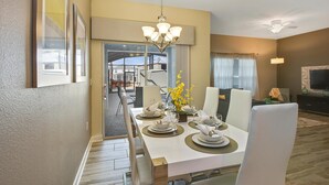 A dining area with a white table set for six, a chandelier, and a view of the outside. - 1579mvd-the Retreat at Champions Gate (Davenport)
