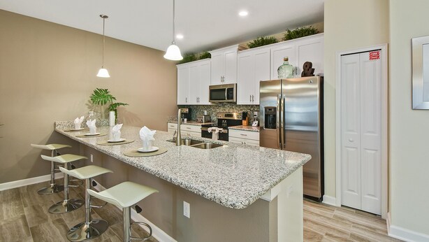A modern kitchen with a granite countertop, stainless steel appliances, and a bar area with stools. - 1579mvd-the Retreat at Champions Gate (Davenport)