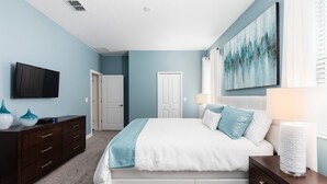 Une chambre à coucher avec un lit, une commode, un téléviseur et des œuvres d’art accrochées au mur.