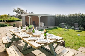 Enclosed sun trap garden with large outdoor dining table set for eleven, lawn and garden storage cabin at luxury holiday home in Rhosneigr, Anglesey - Sand Dollar: family-friendly holiday home in Rhosneigr (Rhosneigr)