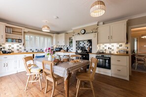 A kitchen with wooden flooring, white cabinetry, a dining table with chairs, and hanging wicker light fixtures. - Sand Dollar: family-friendly holiday home in Rhosneigr (Rhosneigr)
