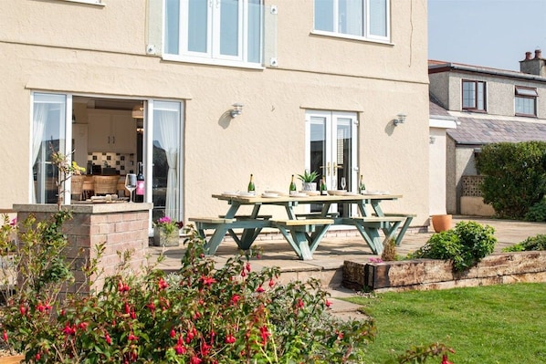 A two-story house with a patio area featuring a wooden table and chairs. - Sand Dollar: family-friendly holiday home in Rhosneigr (Rhosneigr)