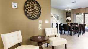 A dining area with a round table, two white cushioned chairs, a vase with flowers, and a decorative wall piece. - 1424ww - The Retreat at Championsgate (Davenport)