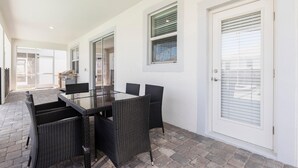 Eine Terrasse mit Tischplatte aus Glas und schwarzen Korbstühlen, eine weiße Tür mit Fenster sowie ein Terraboden aus Ziegelsteinen.