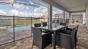 A covered patio with a glass table and chairs, overlooking a swimming pool and a grassy area. - 1521fd - The Retreat at Championsgate (Davenport)