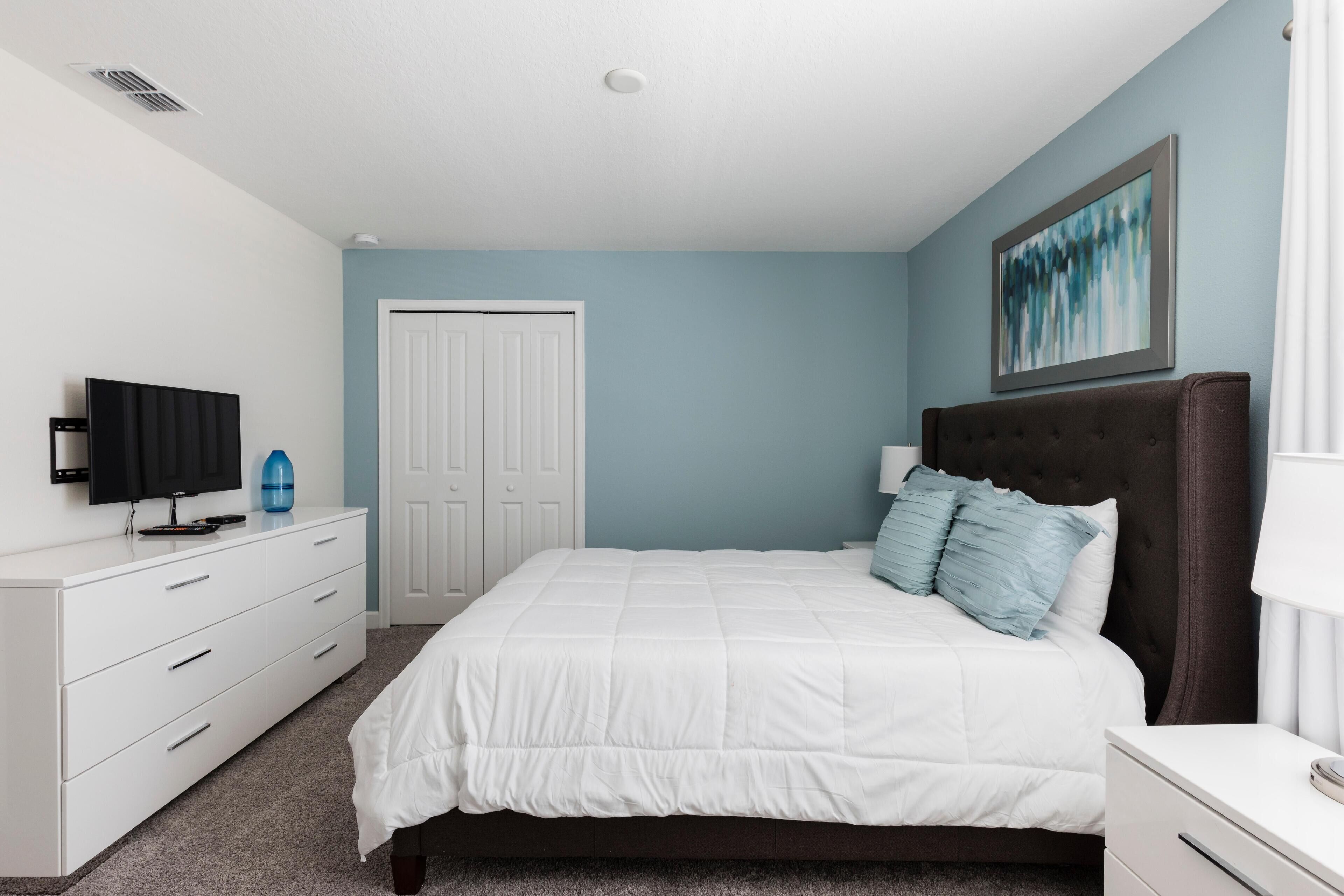 A bedroom with a bed, a dresser, a television, and a door.