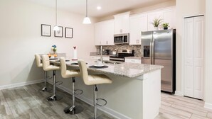 A modern kitchen with white cabinets, stainless steel appliances, and a granite countertop island with bar stools.