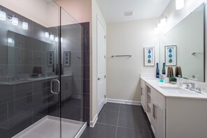 A modern bathroom with a glass shower enclosure, a large mirror, and a vanity with a sink and countertop. - 4741ctd- Storey Lake (Kissimmee)