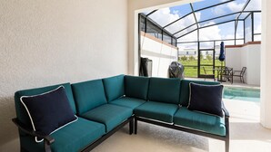 A teal sectional sofa with dark cushions in a bright room with a large glass door leading to an outdoor patio area. - 8919sid-the Retreat at Championsgate (Davenport)