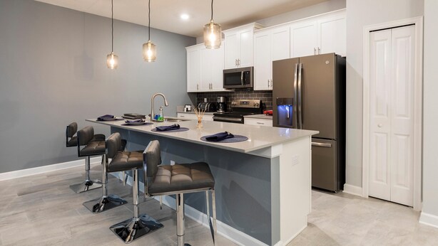 A modern kitchen with white cabinets, stainless steel appliances, and bar stools. - 8919sid-the Retreat at Championsgate (Davenport)