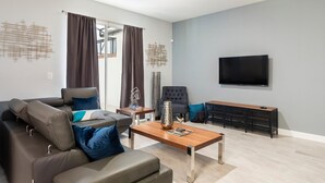 A modern living room with a sectional sofa, a coffee table, a TV, and a seating area with a bench. - 8919sid-the Retreat at Championsgate (Davenport)