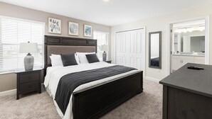 A bedroom with a dark wood bed, white bedding, a nightstand with a lamp, a dresser, and a large mirror. - 8919sid-the Retreat at Championsgate (Davenport)
