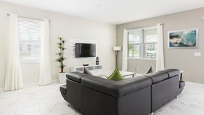 Un salon moderne avec un canapé gris foncé, un téléviseur à écran plat, une console blanche et une plante en pot.