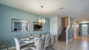 Un espace repas avec une table dressée pour six personnes, un lustre et un escalier menant à un autre niveau.