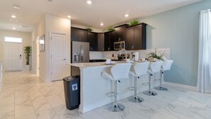 A modern kitchen with dark cabinets, a white island with bar stools, and a stainless steel refrigerator. - 1559pw NON Renting 8/15/21the Retreat at Championsgate (Davenport)
