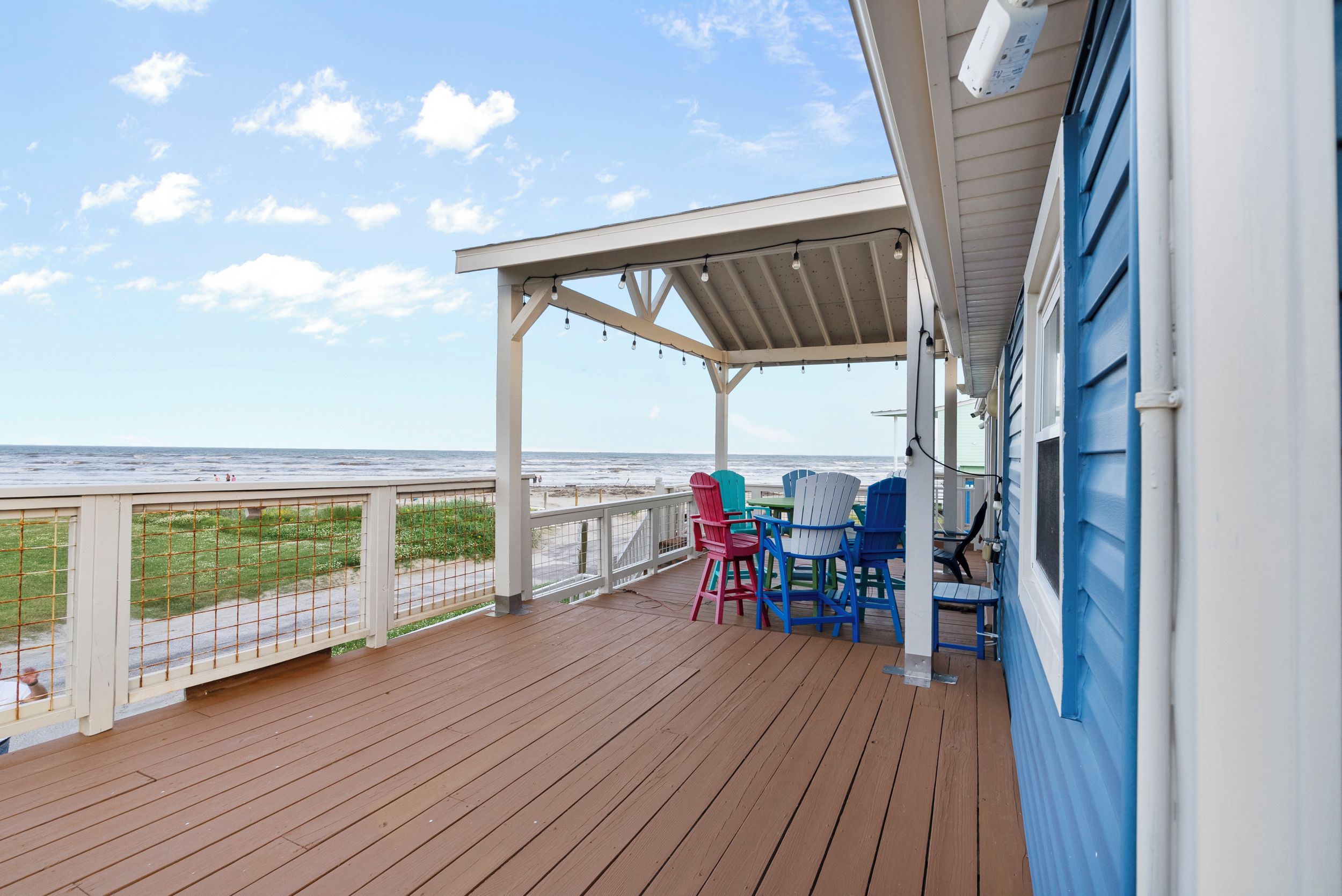 A wooden deck with a covered area, outdoor seating, and a view of the ocean.