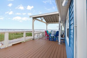 Una terraza de madera con zona cubierta, asientos exteriores y vista al océano.