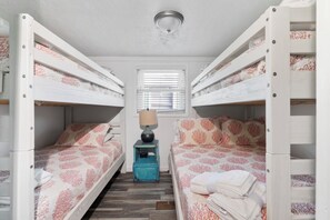 A bunk bed room with a window, a lamp, and a small table.
