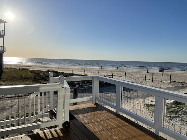 A wooden deck with a white railing overlooking a beach.