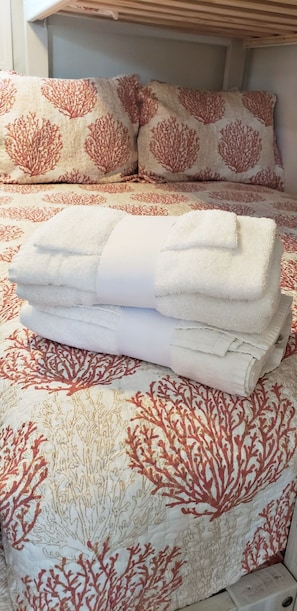A neatly folded stack of white towels on a bed with a coral-patterned bedspread.