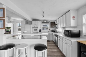 A modern kitchen with white cabinetry, a central island with stools, and a microwave.