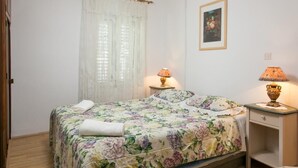 Un dormitorio con colcha estampada, dos lámparas de noche, un cuadro en la pared y una ventana con cortinas traslúcidas.