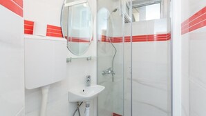 Un baño moderno con cabina de ducha de vidrio, un lavamanos blanco y un espejo.