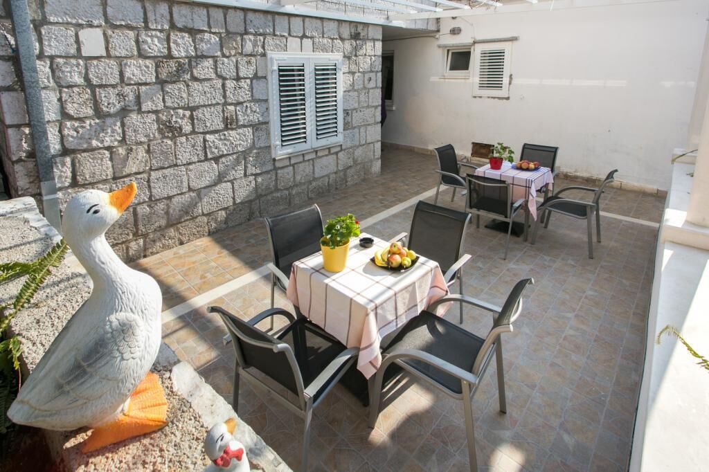 A stone building with a patio area featuring a table with chairs, a potted plant, and a fruit bowl.