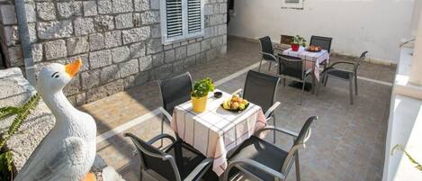 A stone building with a patio area featuring a table with chairs, a potted plant, and a fruit bowl.