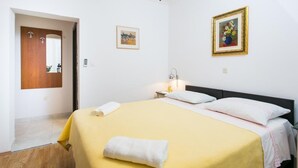 A hotel room with a bed, a nightstand, a lamp, and a painting on the wall. - Guest House Kusalo- Basic Triple Room with Patio (Dubrovnik)