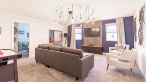 A modern living room with a grey sectional sofa, a white armchair, a flat-screen TV, and a unique chandelier.