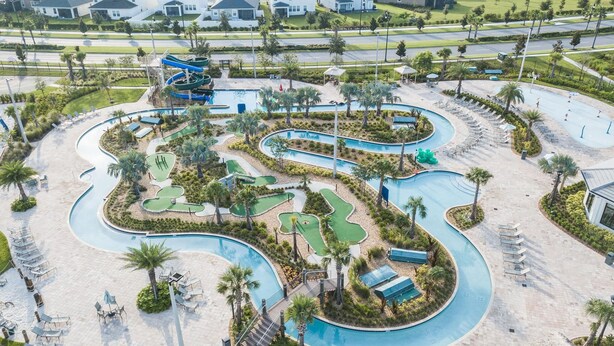 An aerial view of a resort with a winding pool, multiple green areas, and a large water slide.