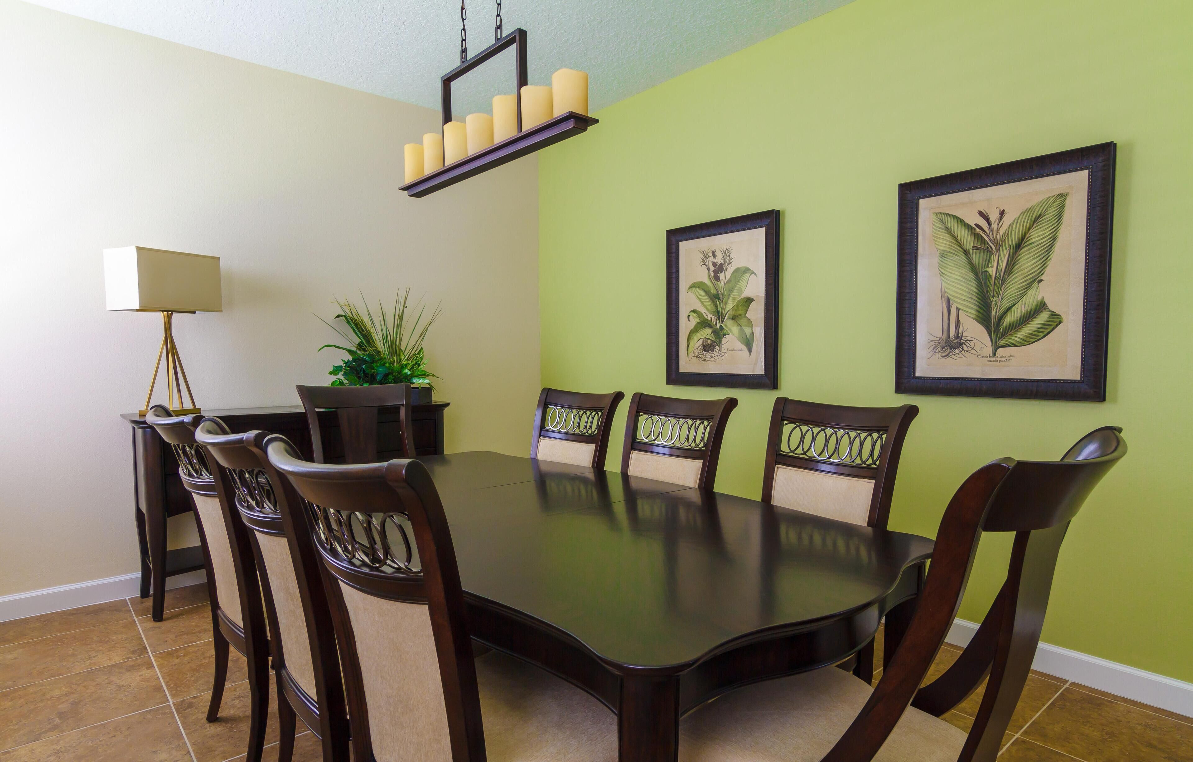 Un coin repas avec une table ronde, six chaises, une plante en pot, un lampadaire et des reproductions botaniques encadrées accrochées au mur.