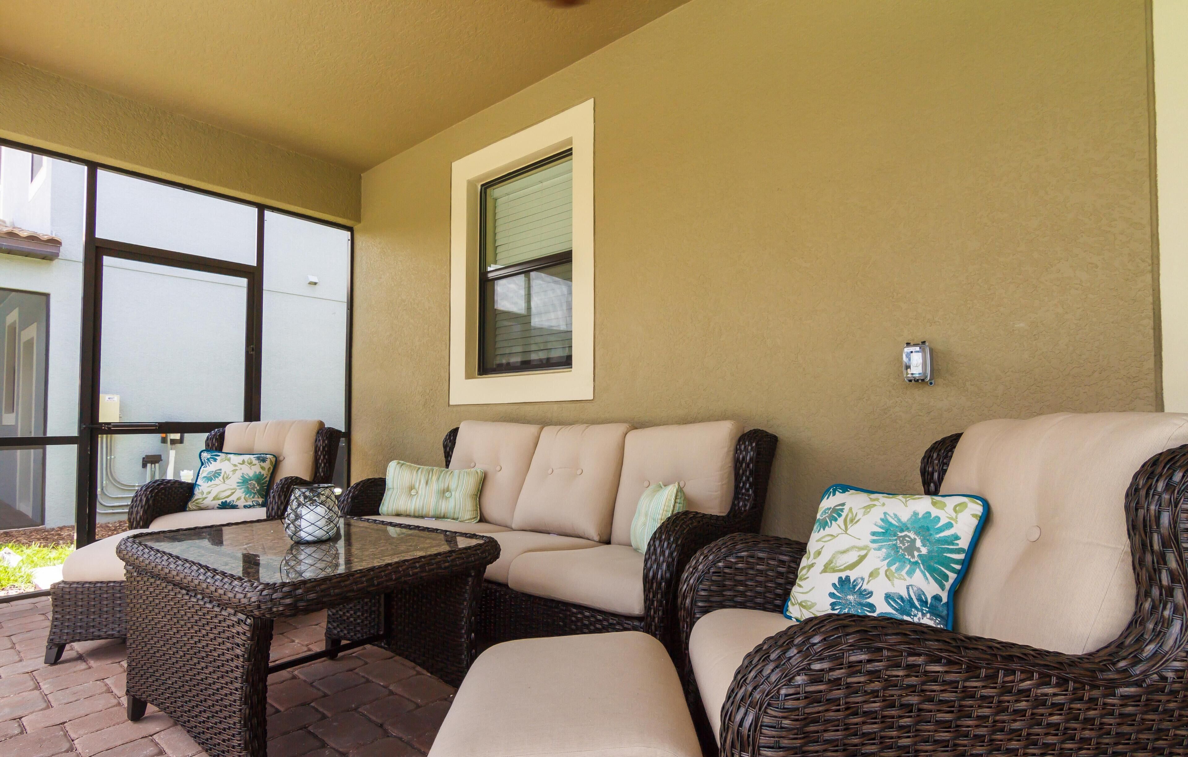 A covered patio area with wicker furniture, including sofas and a table, and a window with blinds.