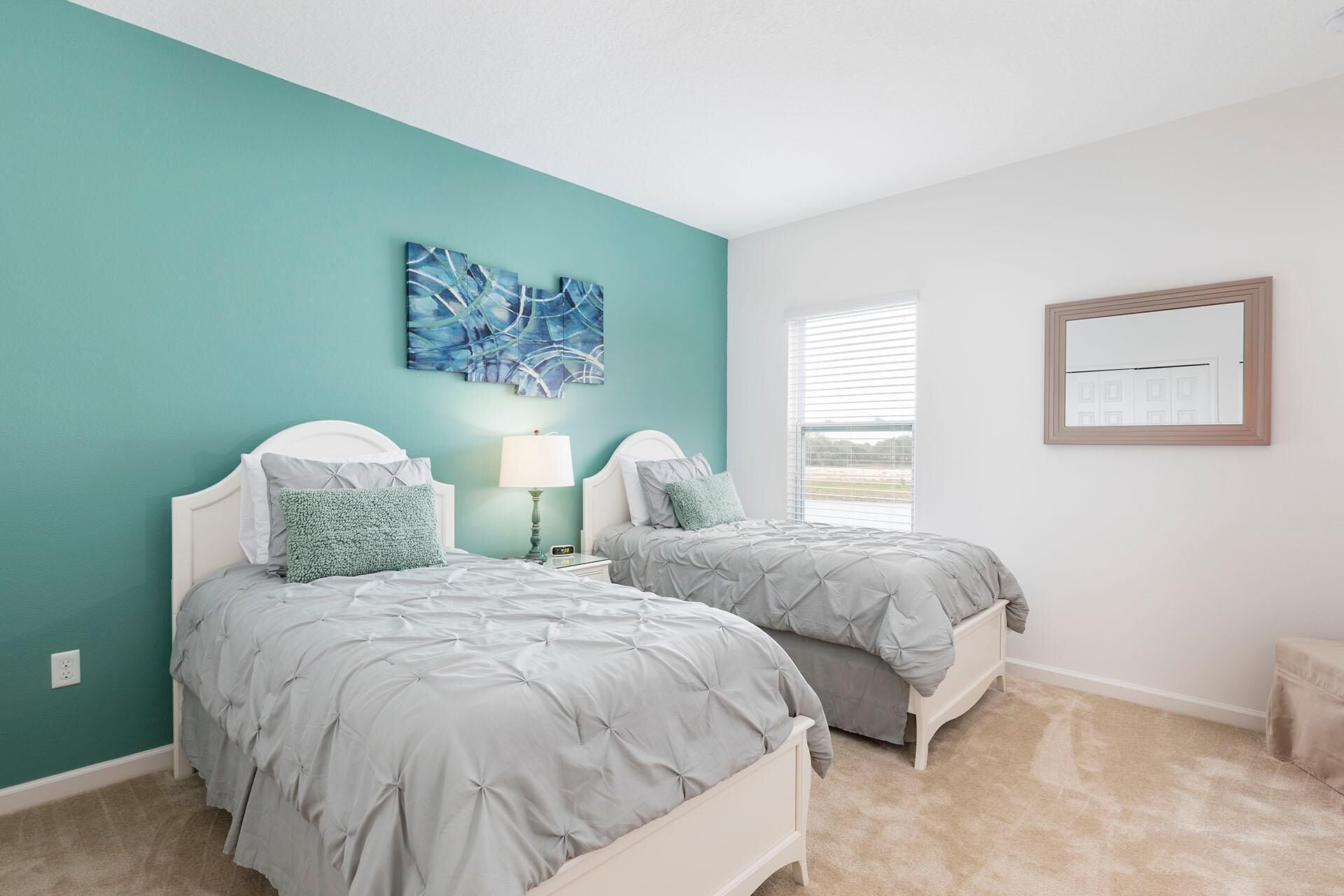 A bedroom with two beds, teal walls, and a large window.