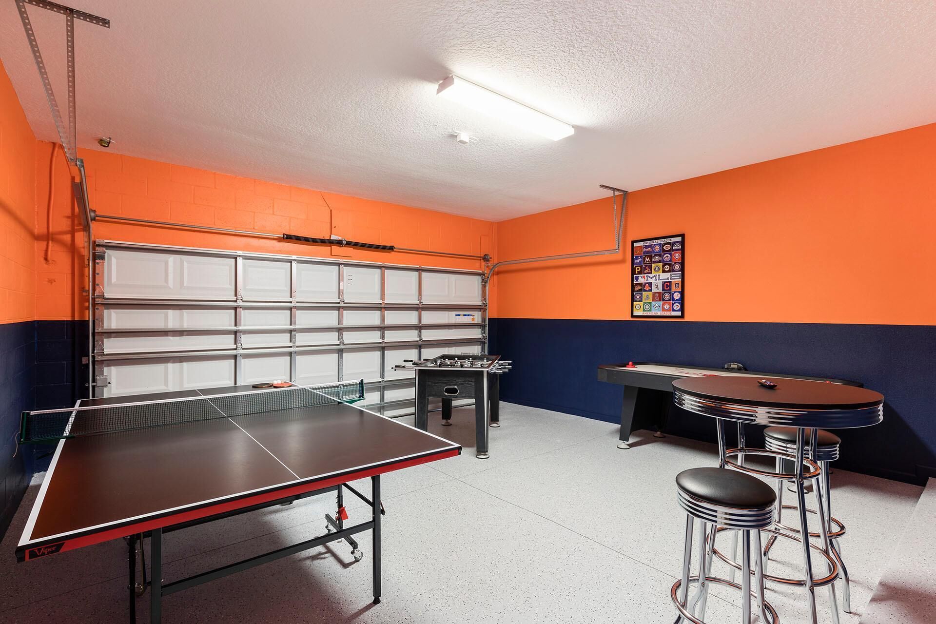 A room with a ping pong table, a foosball table, and a bar area with stools.