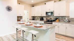 A modern kitchen with white cabinets, granite countertops, a central island with bar stools, and stainless steel appliances. - 1576tl-the Retreat at Champions Gate (Davenport)