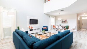 A modern living room with a sectional sofa, a glass coffee table, and a flat-screen TV mounted on the wall. - 1576tl-the Retreat at Champions Gate (Davenport)