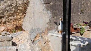Un mur de pierre surmonté d’une statuette d’oiseau posée sur un piédestal et d’un jardinière remplie de fleurs.