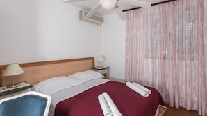 Une chambre d’hôtel avec un lit, un ventilateur de plafond, une table de chevet avec une lampe, une chaise et une fenêtre avec des rideaux.