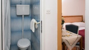 Une salle de bain avec des toilettes, une douche et une petite table recouverte d’une nappe.