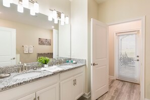 A bathroom with a granite countertop, white cabinets, a large mirror, and a door with blinds. - 9042sid- The Retreat at Championsgate (Davenport)